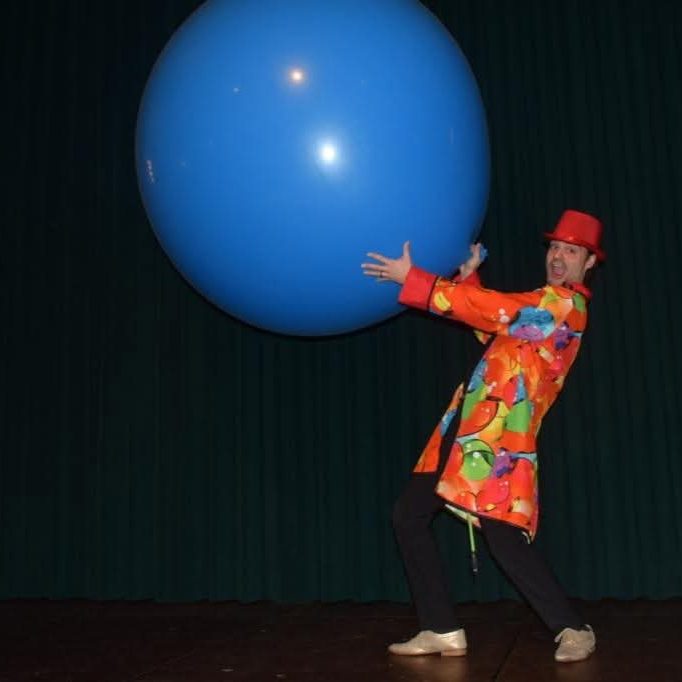Kinderzauberer Maik mit großem Ballon Kinderzauberer im bunten Kostüm hebt einen großen blauen Ballon in die Luft.